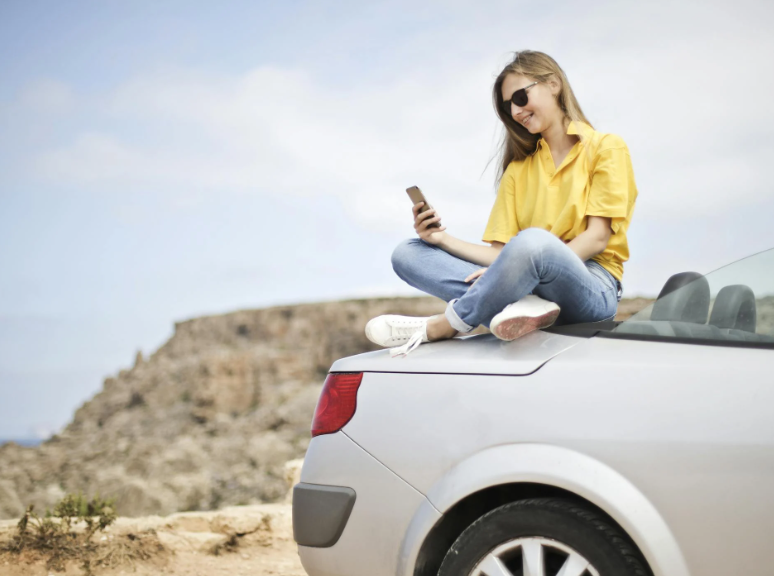 Kvinde sidder på en bil og benytter sin mobil - duka