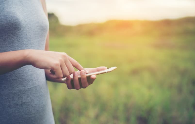 Mobilabonnement og bæredygtighed - kvinde står i naturen på en mark med sin mobil